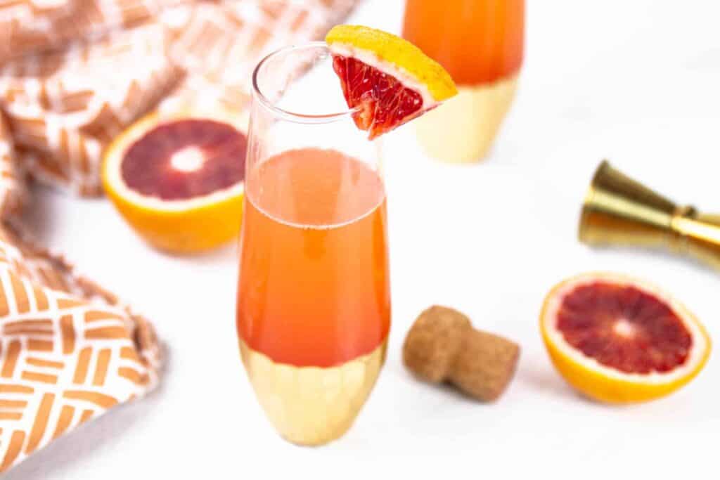 A blood orange wedge on a champagne flute containing a red cocktail.