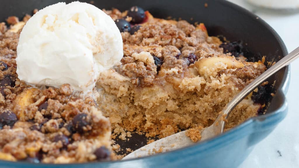 Blueberry peach buckle in cast iron skillet with scoop of vanilla ice cream.