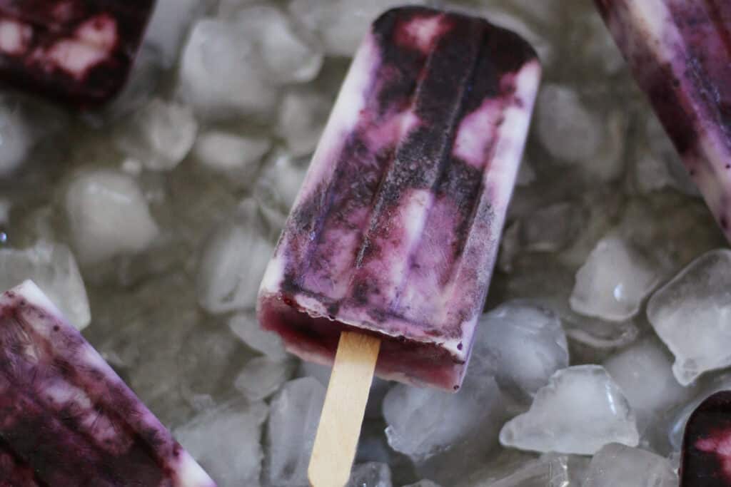 Yogurt and blueberry popsicles on a sheet pan with ice cubes.