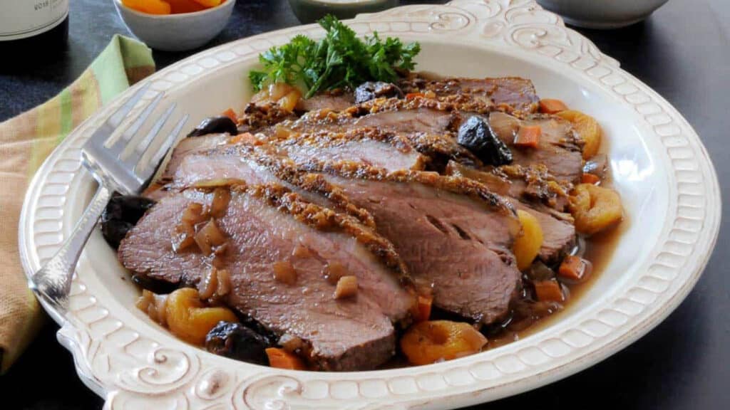 Slices of brisket with dried fruit and herbs on a white platter.