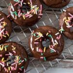 Chocolate cake mix donuts with colorful sprinkles on a baking rack.