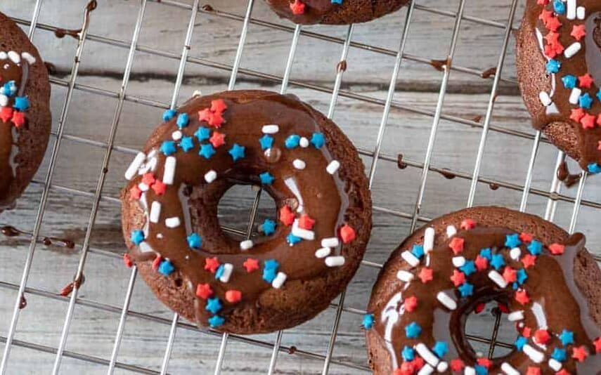 Chocolate cake mix donuts on a cooling rack with chocolate glaze and red, white and blue sprinkles.