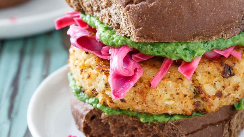 Cheddar cauliflower burger with pickled cabbage and pesto on a plate.