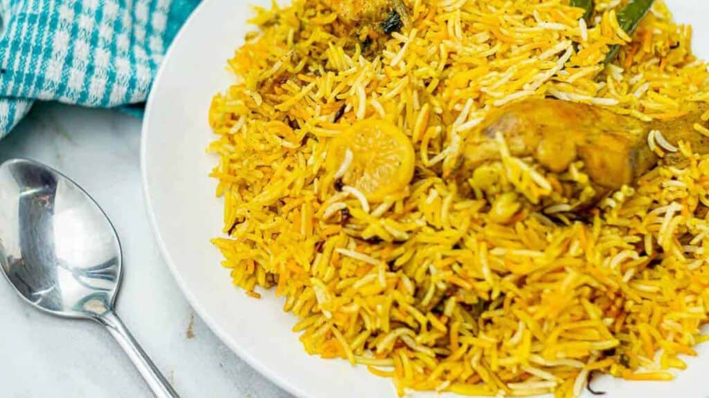 Chicken biryani on a plate with a spoon and blue and white napkin on the side..