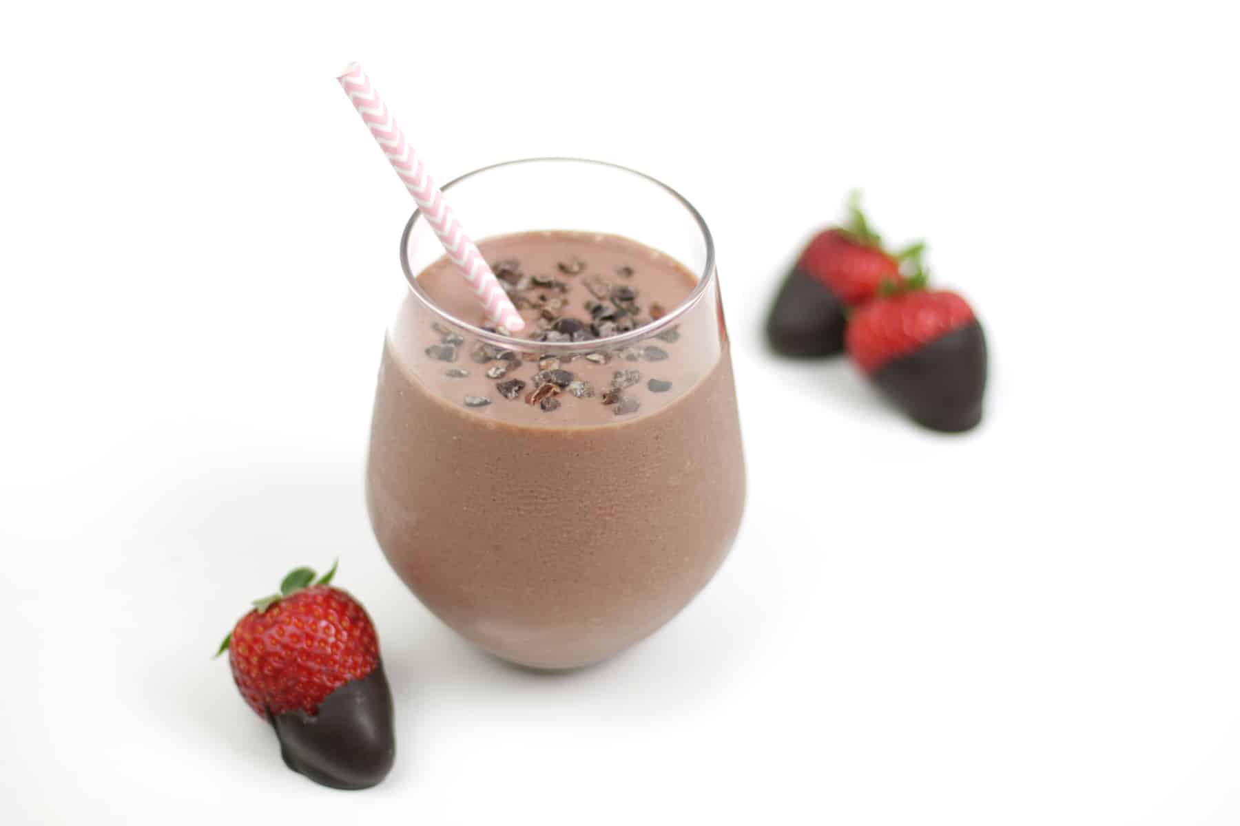 a Chocolate Covered Strawberry Smoothie in a stemless wine glass with a cocoa nib topping and next to three chocolate covered strawberries.