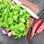 Cilantro, garlic, and chilis on a wooden cutting board.