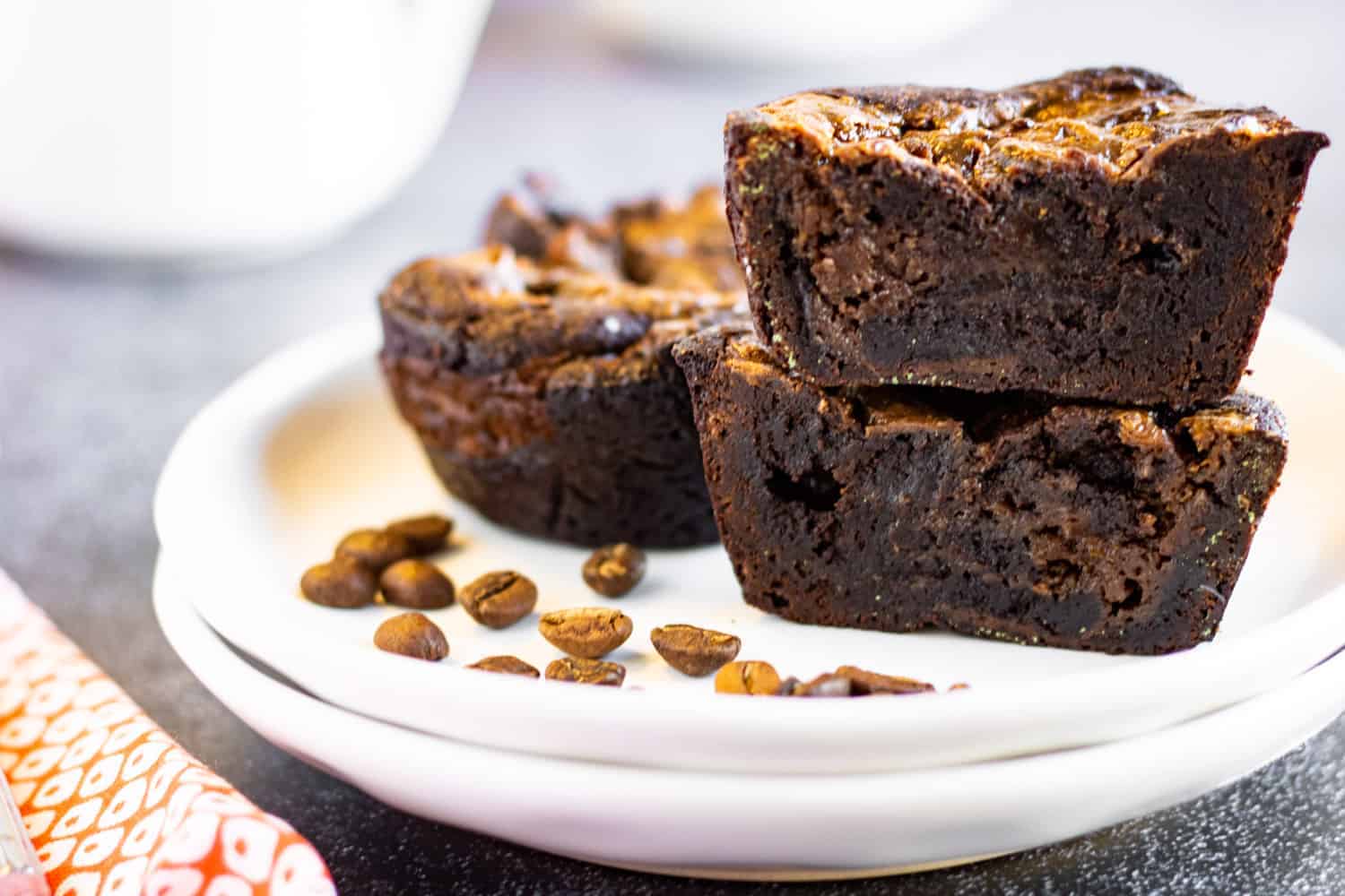 Coffee brownies on a plate with coffee beans on the plate too.