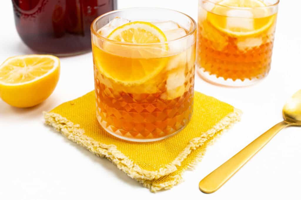 lemons garnishing a glass of ice tea next to a mason jar pitcher of tea.