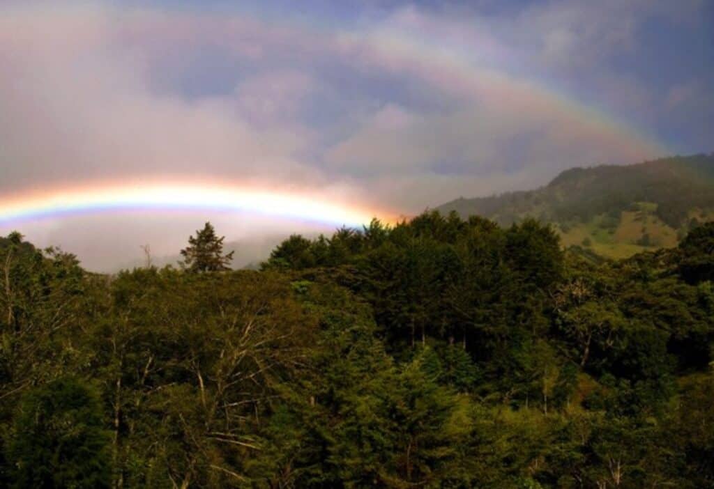 A double rainbow in the sky above green mountains in Costa Rica.