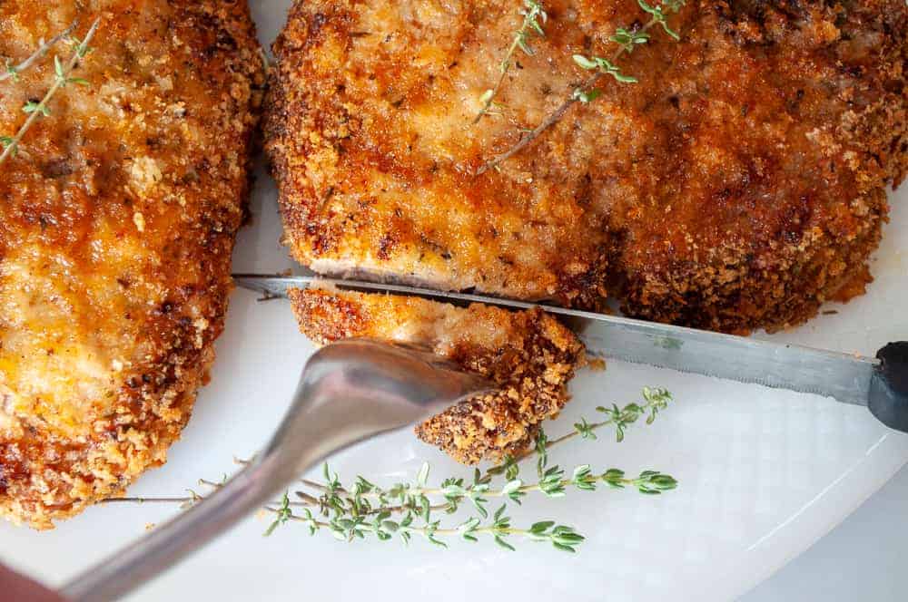 Slicing into a crispy pork chop with thyme on the side.