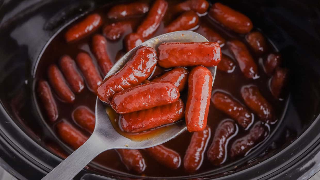 Crock pot little smokies on a spoon over the slow cooker.