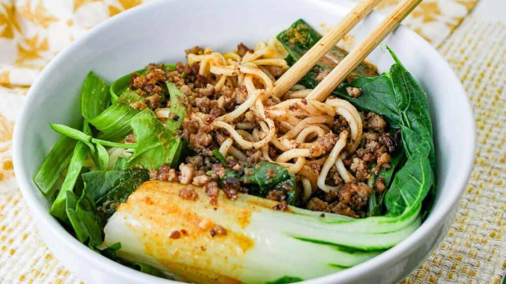 Dan dan noodles with bok choy in a white bowl with chopsticks.