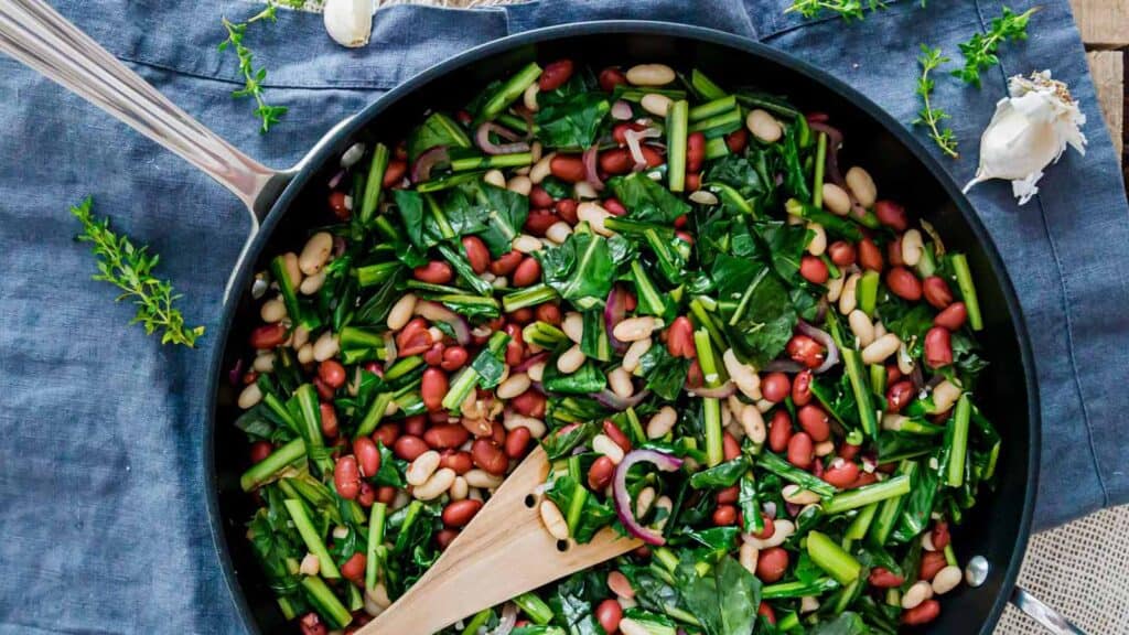 Dandelion greens and beans in a skillet with a wooden spatula.