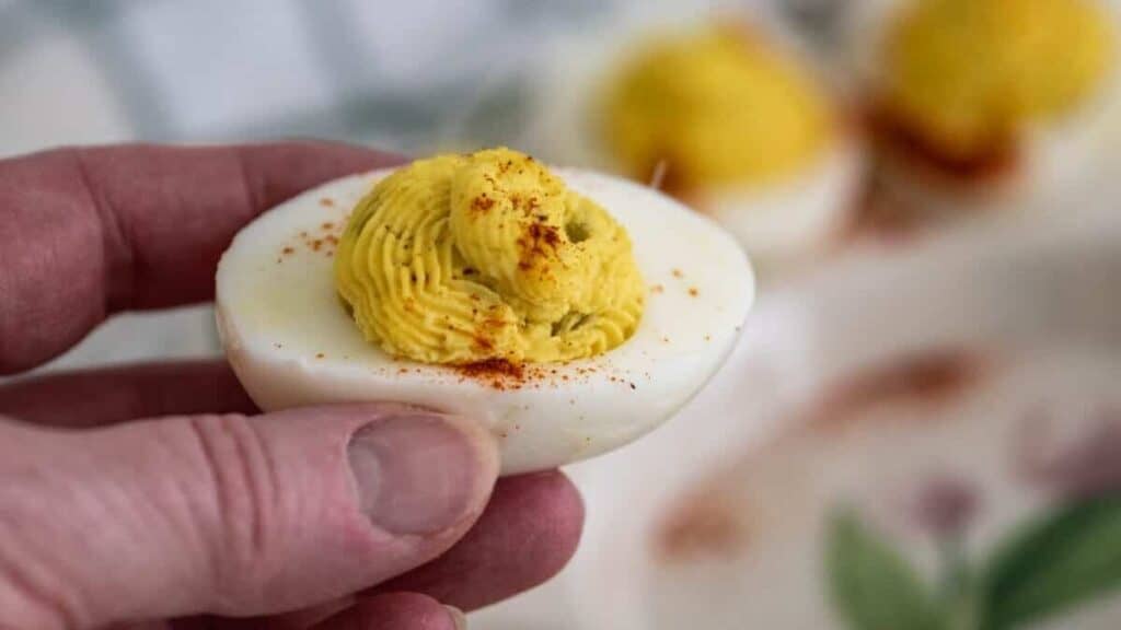 Holding a deviled egg sprinkled with paprika.