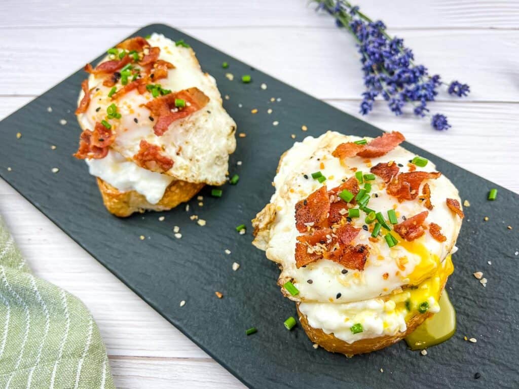 Cottage Cheese Toasts with Sunny-side Up Eggs and Bacon on a black platter.