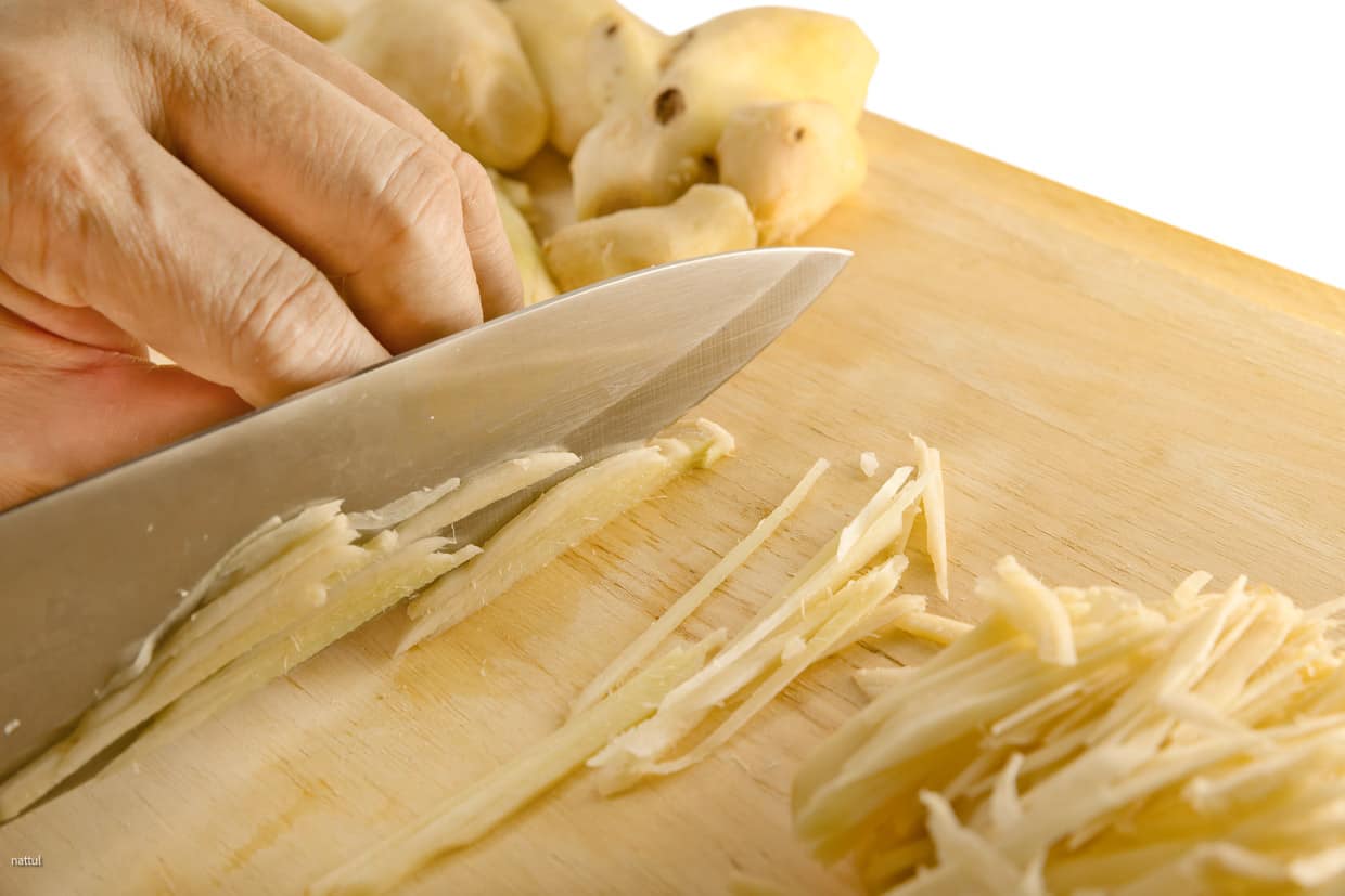 Fresh ginger being cut into slivers with a chef's knife.