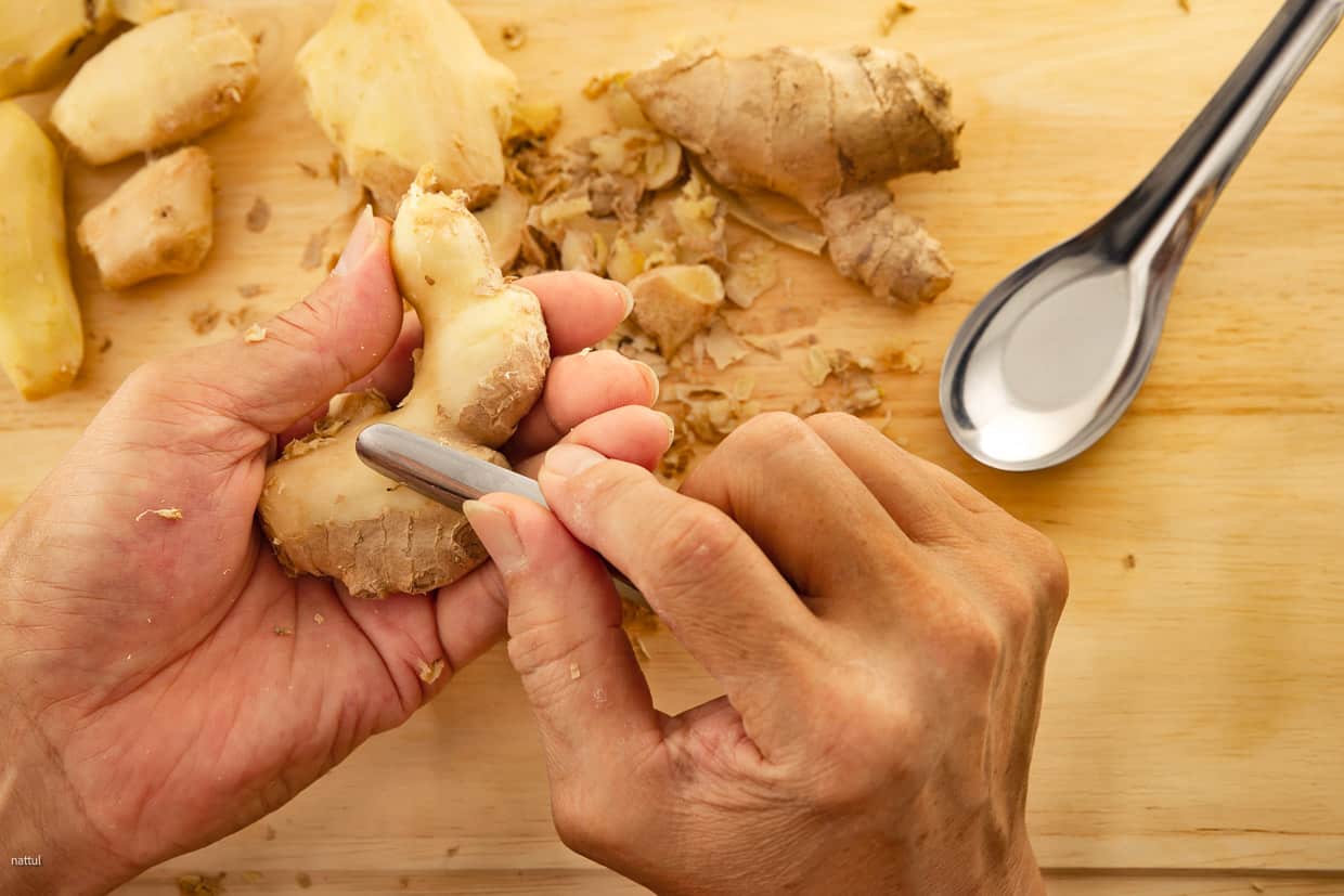 Fresh ginger being peeled with a spoon.