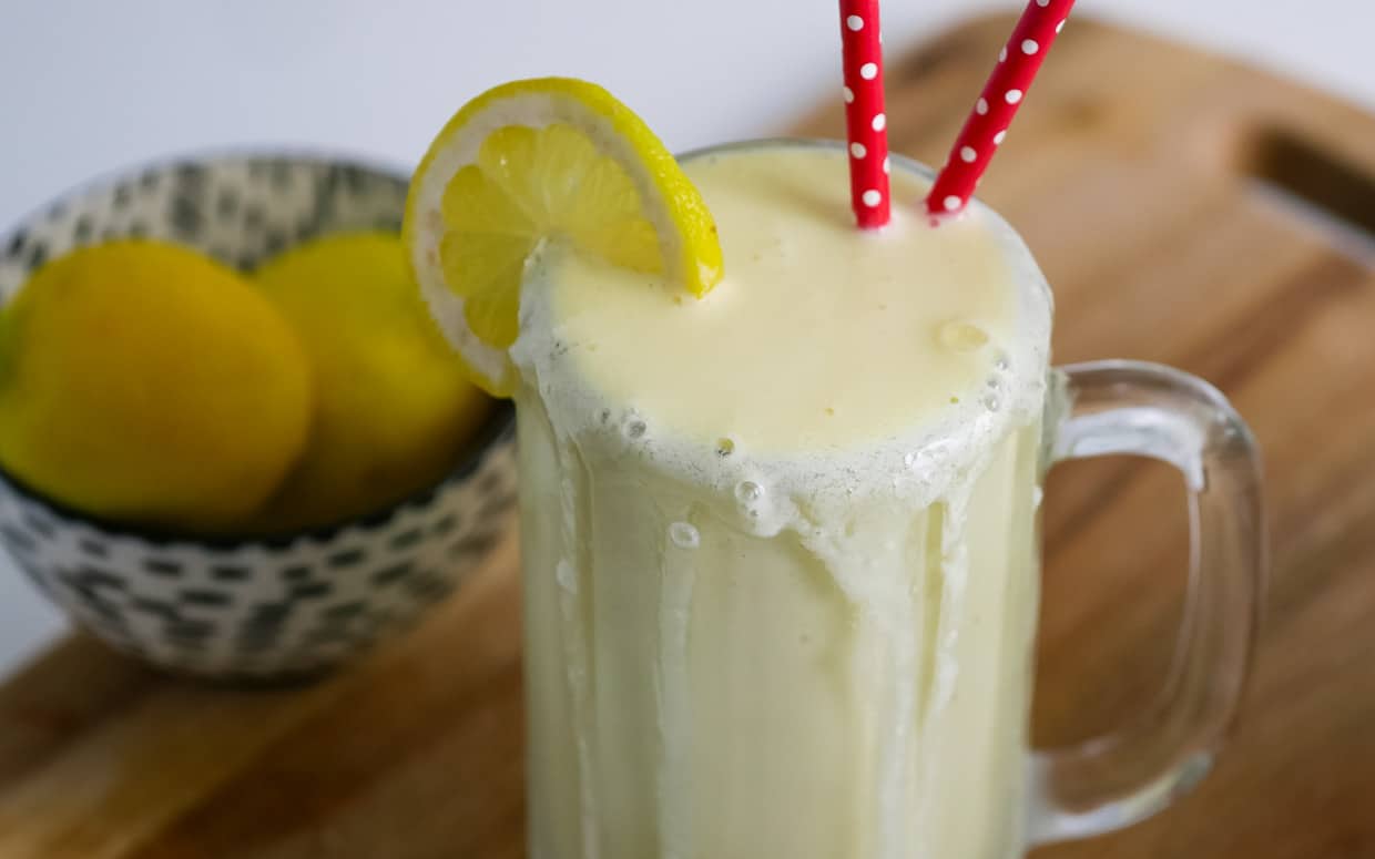 Closeup of a mug of frosted lemonade with a slice of lemon and two red straws.