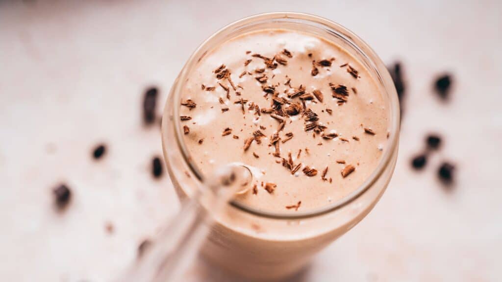 Top view of a clear glass filled with a frozen brown shake garnished with chocolate shavings.