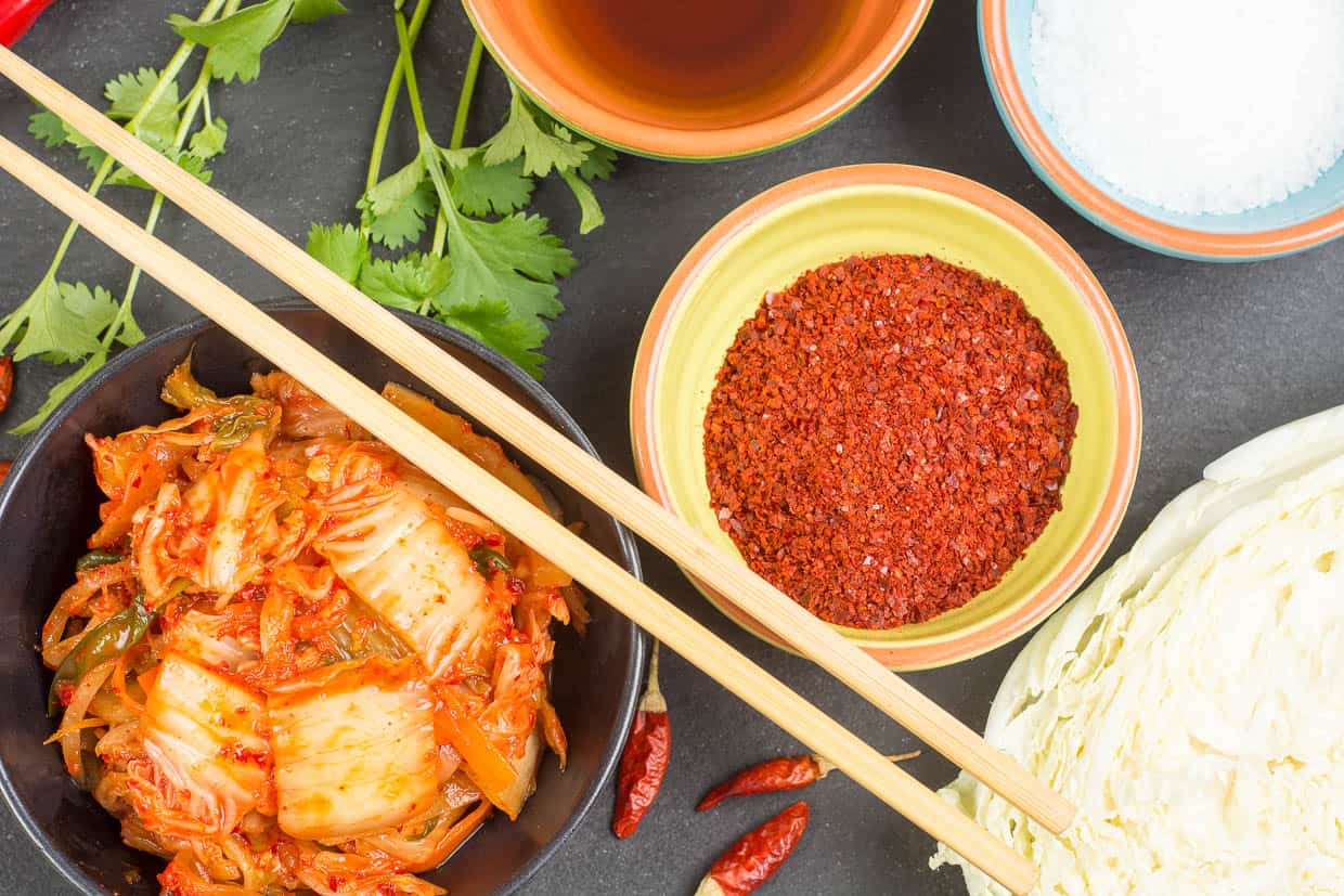 Overhead shot showing kimchi in a bowl with chopsticks, a bowl of gochugaru.