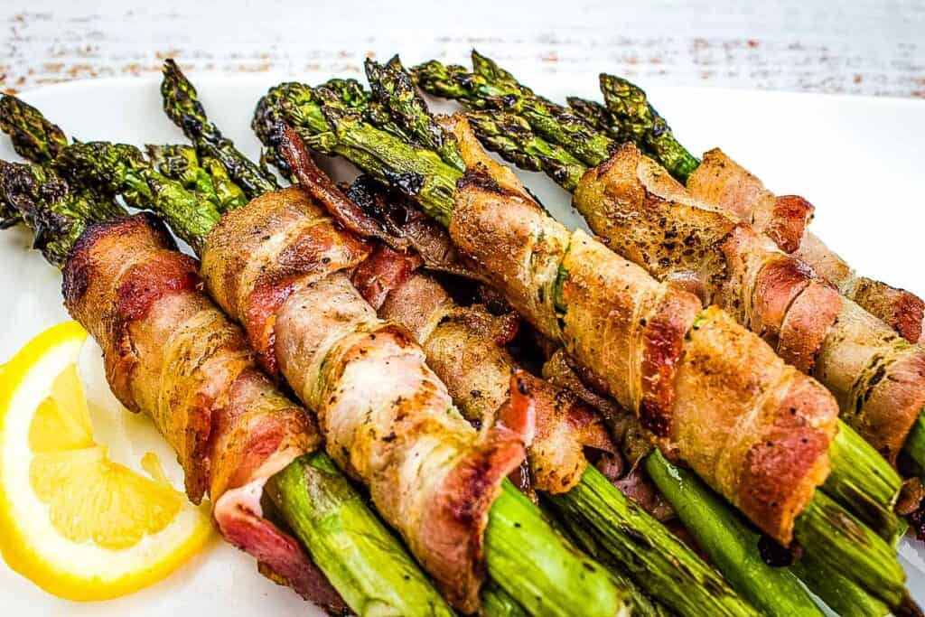 A closeup shot of Grilled Bacon Wrapped Asparagus on a white plate.