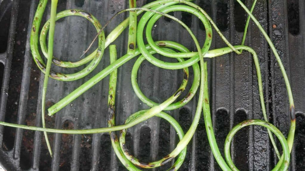 Curly garlic scapes cooking on a grill.