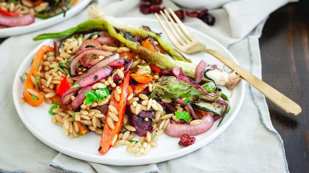 Grilled summer vegetables with orzo on a white plate with a fork.