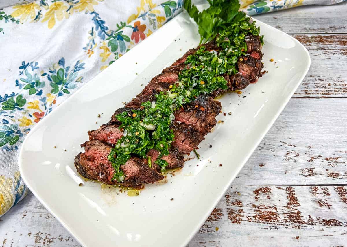 Sliced Grilled Hanger Steak with Chimichurri on a white plate.