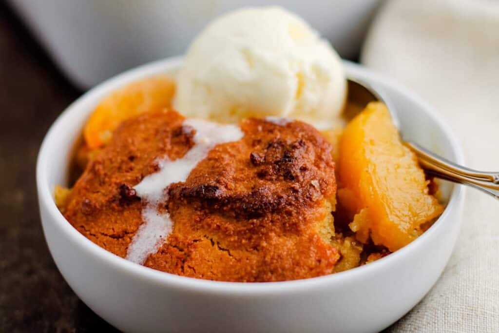 A bowl of Healthy Peach Cobbler with ice cream melting on top.