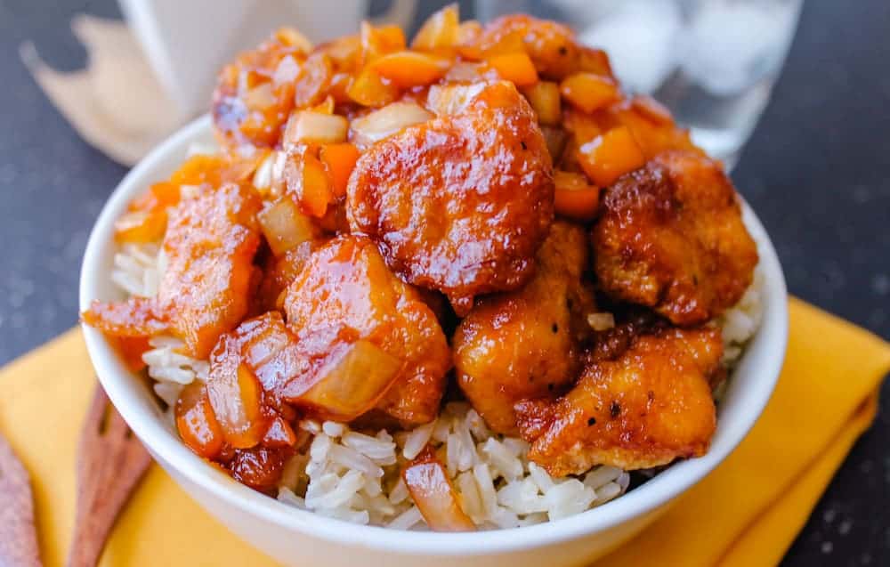 A bowl of sweet and sour chicken over rice.