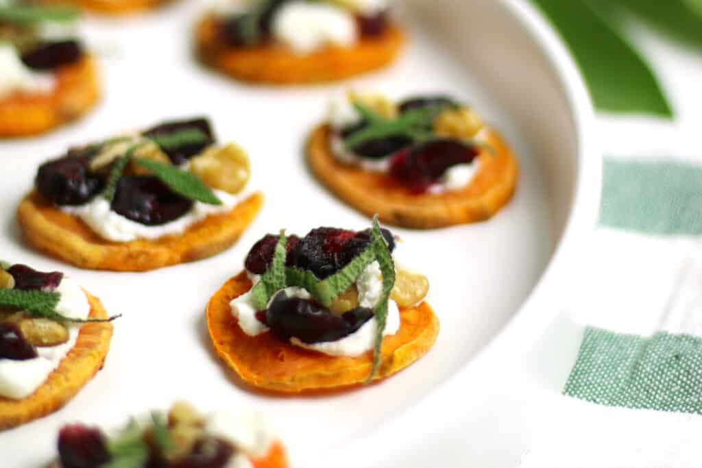 Sweet potato toasts with cheese, cranberries, walnuts and sage on a white plate.