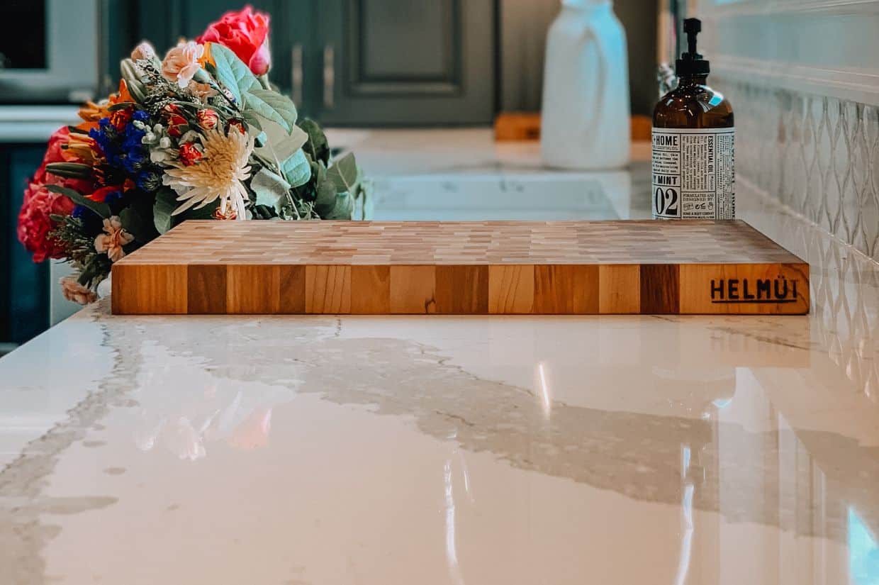 Kitchen quartz countertop with wooden cutting board, flowers, and liquid soap.