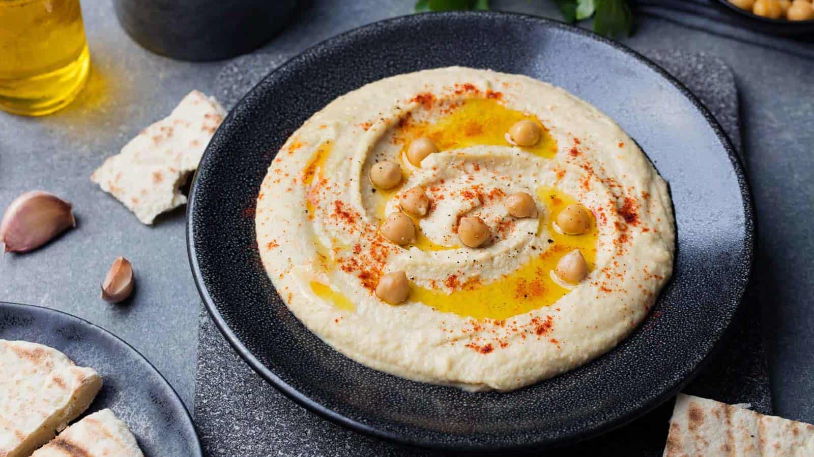 Hummus in a black bowl garnished with whole chickpeas, olive oil, and paprika.
