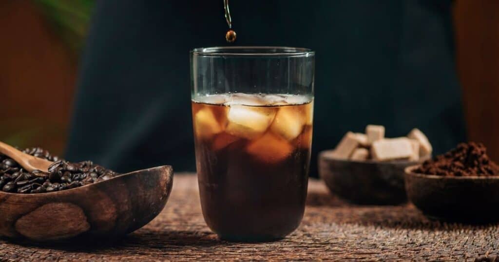 iced americano in glass with bowl of coffee beans.