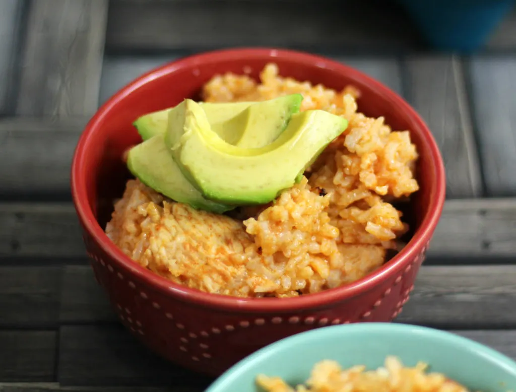 Mexican Chicken and Rice in a red bowl, topped with avocado slices.