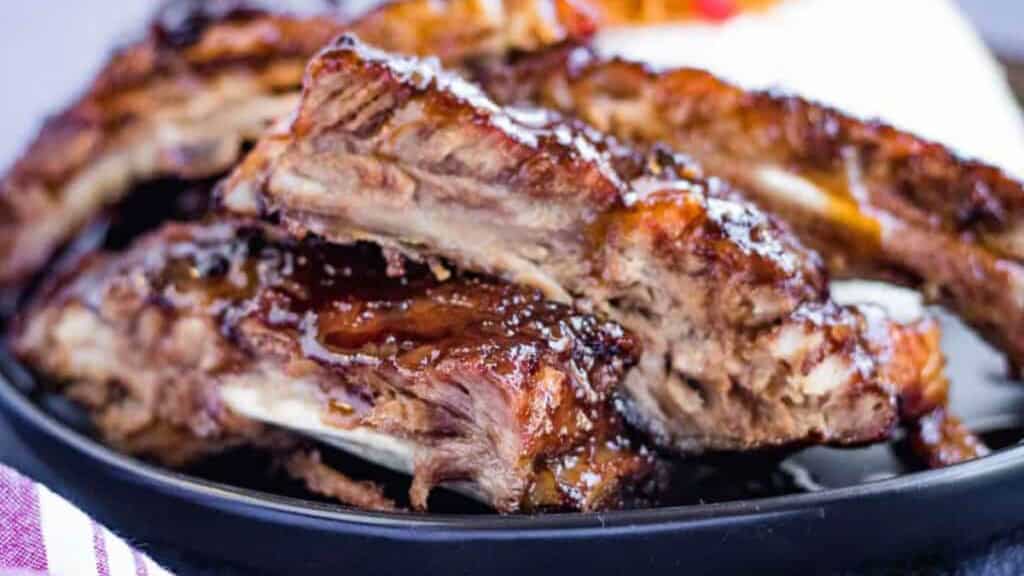 A pile of hoisin glazed spare ribs with rice in the background.