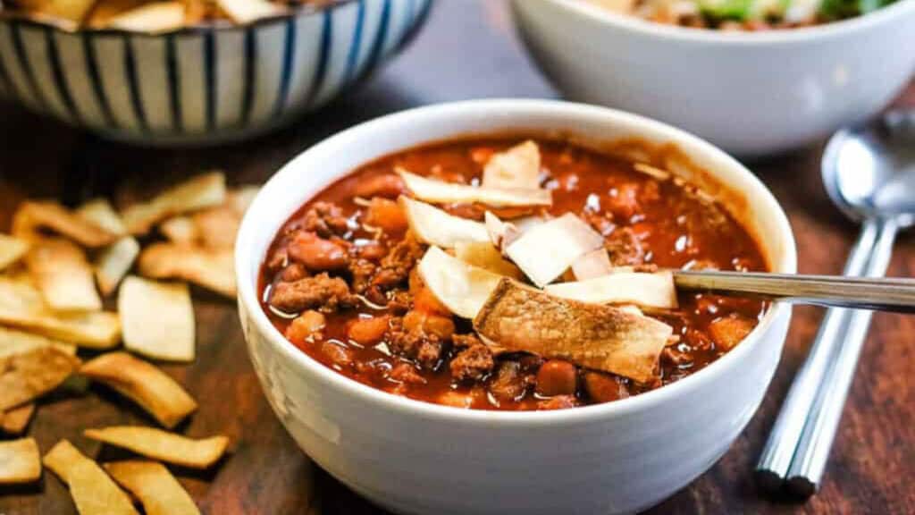 Low angle shot of a white bowl filled with turkey chili and topped with tortilla strips.