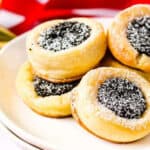 Several poppy seed filled kolacky on a white plate with red and gold ribbons in the background.