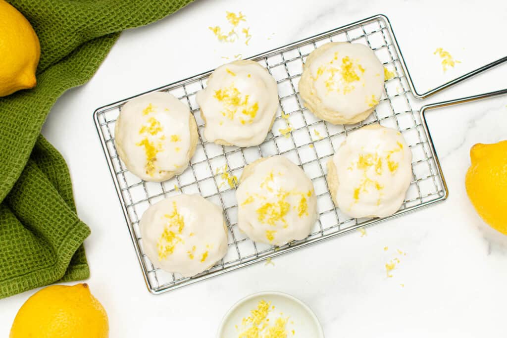 Lemon cookies on a silver cooling rack with lemons around it.
