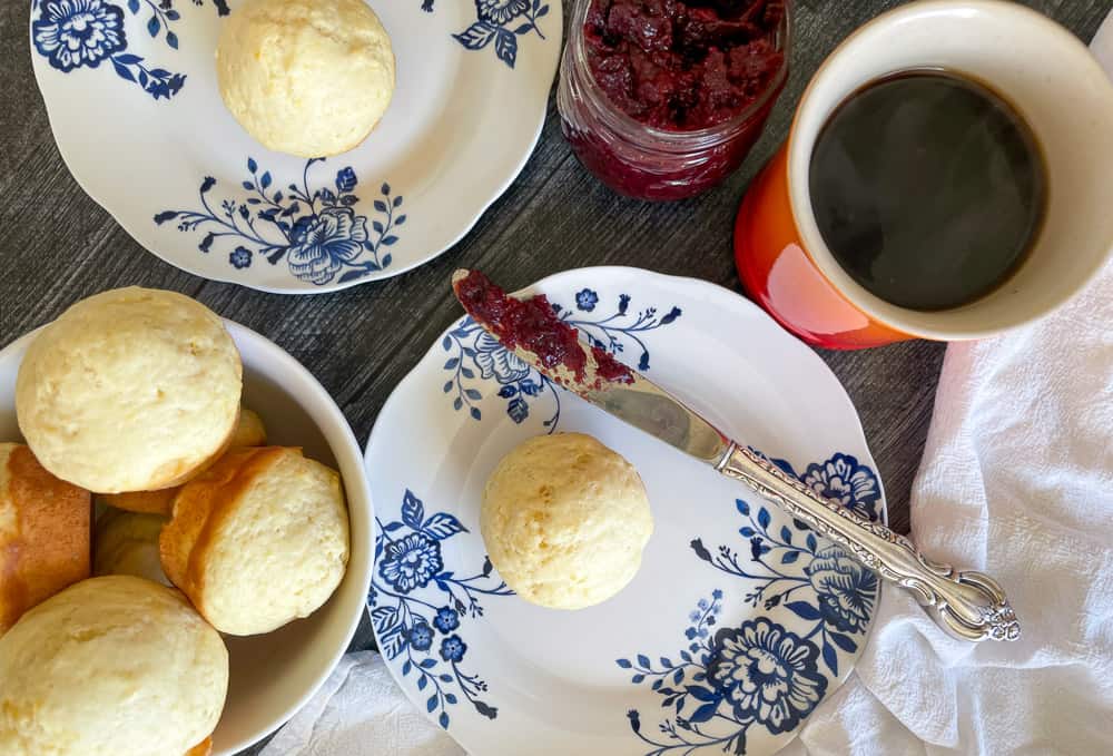 Lemon muffins on blue and white plates with a pot of raspberry jam and a cup of coffee.