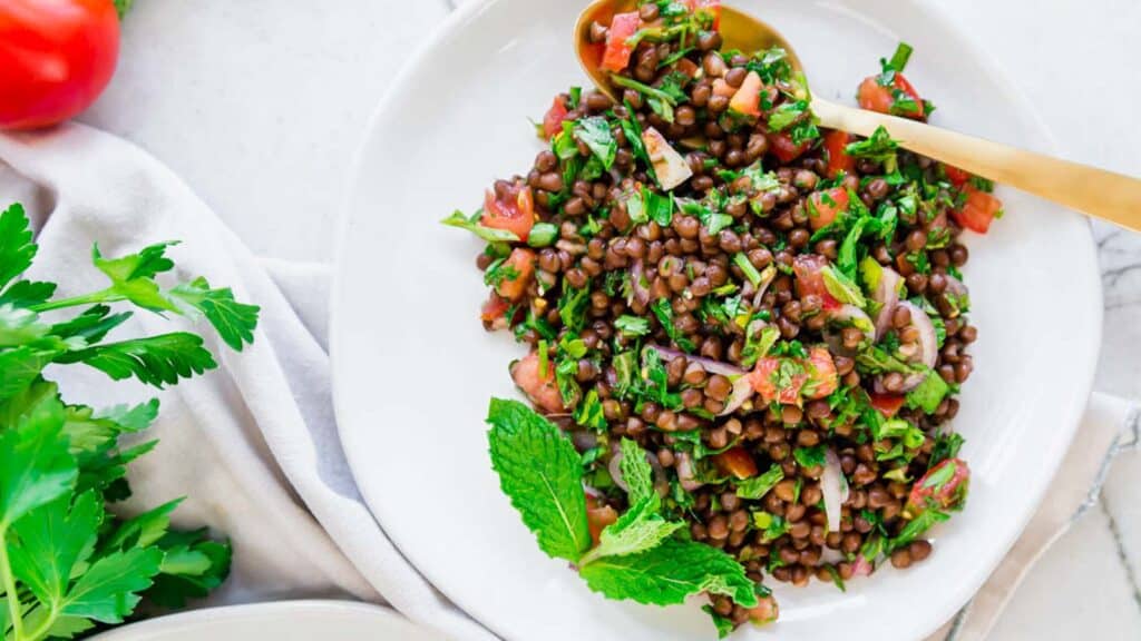Lentil tabbouleh on a white plate with mint garnish and gold spoon.