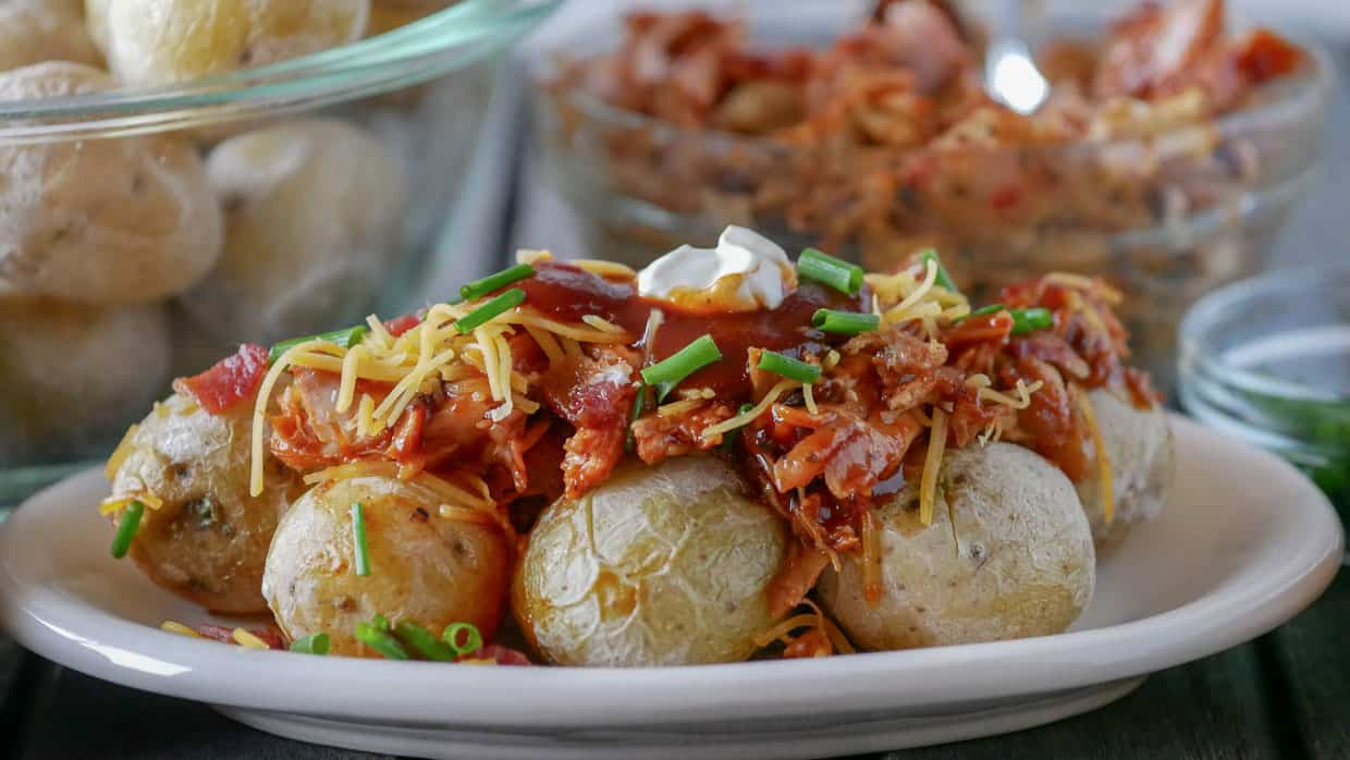 Plate of loaded salt potatoes topped with pulled pork, BBQ sauce, cheese and sour cream.