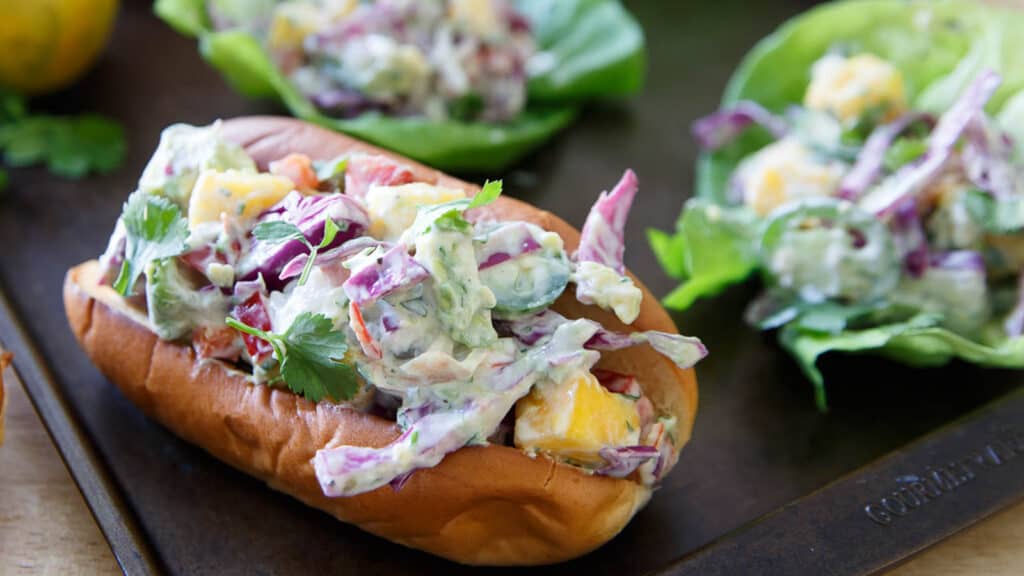 Lobster mango salad in a hot dog bun with lettuce wraps in the background.