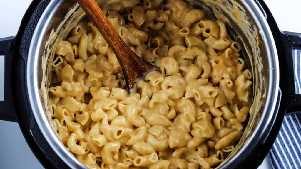 Macaroni and cheese in the instant pot with a wooden spoon.