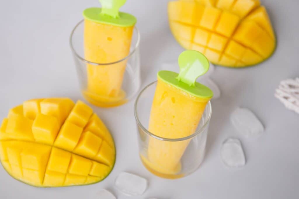 Mango popsicles in a clear glass cup.