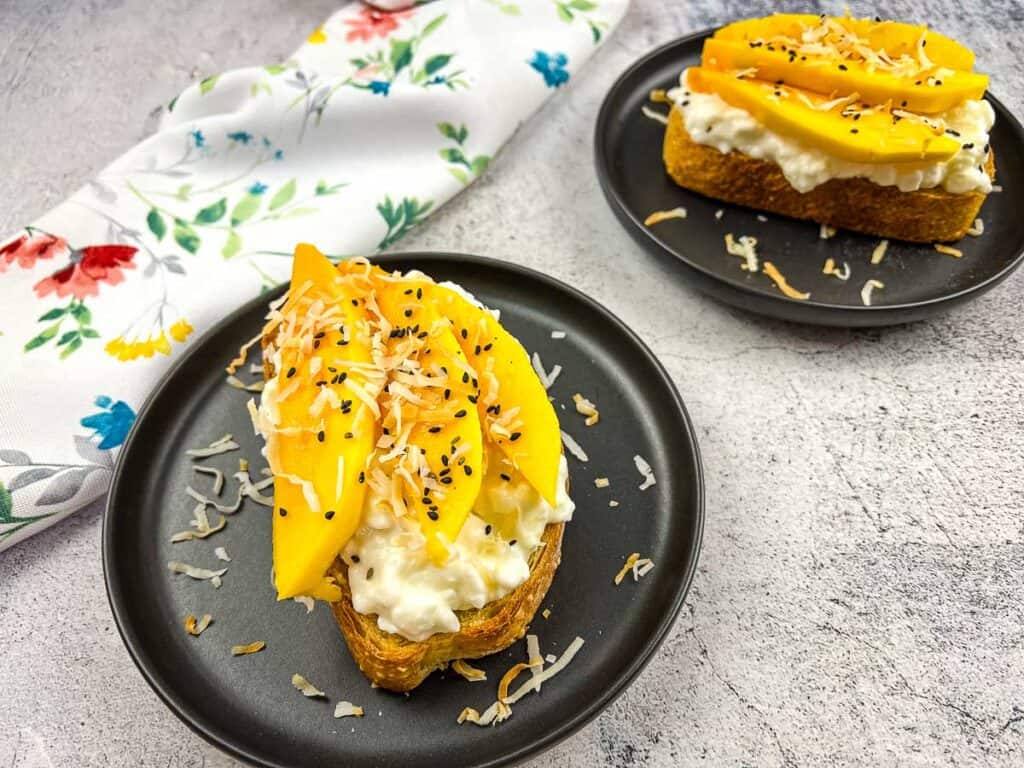 Cottage Cheese Toasts with Mango & Coconut on black plates.