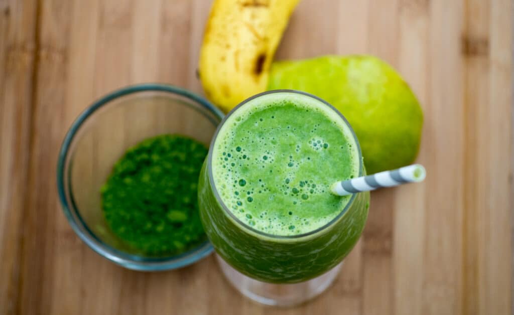 Top view of matcha pear smoothie with pear and match powder on a cutting board.