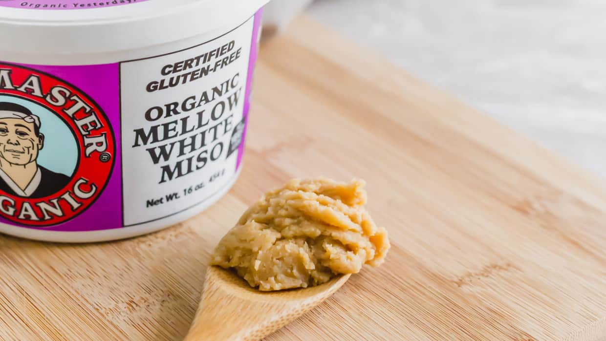 Miso paste on a wooden spoon with tub in the background.