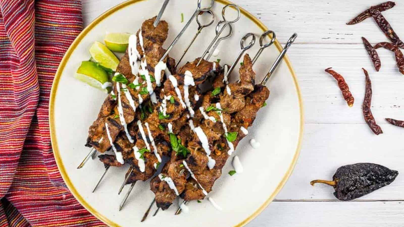 Grilled Steak skewers on a white plate with chilis nearby.