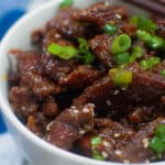 Closeup of crispy beef in a bowl with green onions and sesame seeds.